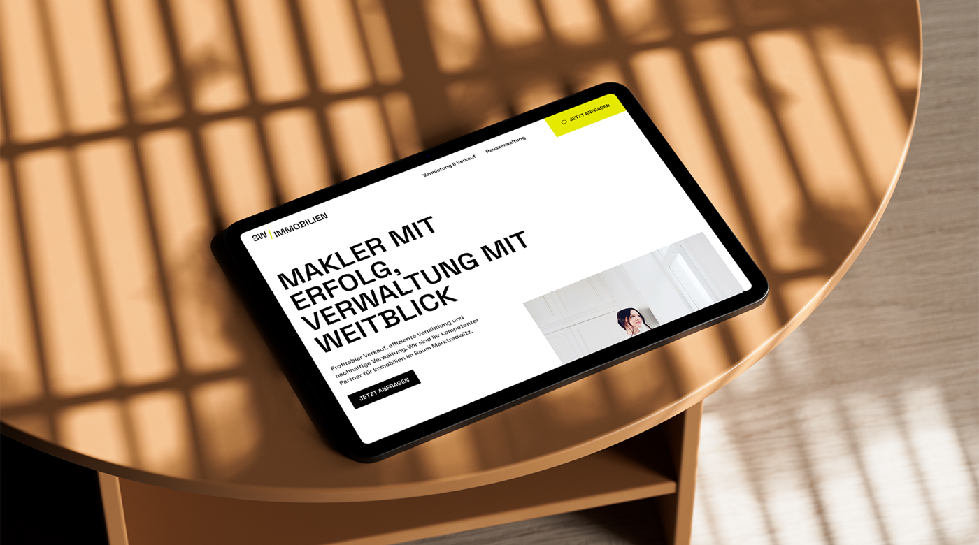 Tablet auf einem runden Holztisch zeigt Webseite mit Text „Makler mit Erfolg. Verwaltung mit Weitblick.“